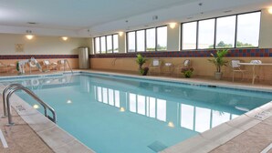 An indoor swimming pool with clear water, surrounded by lounge chairs and potted plants.