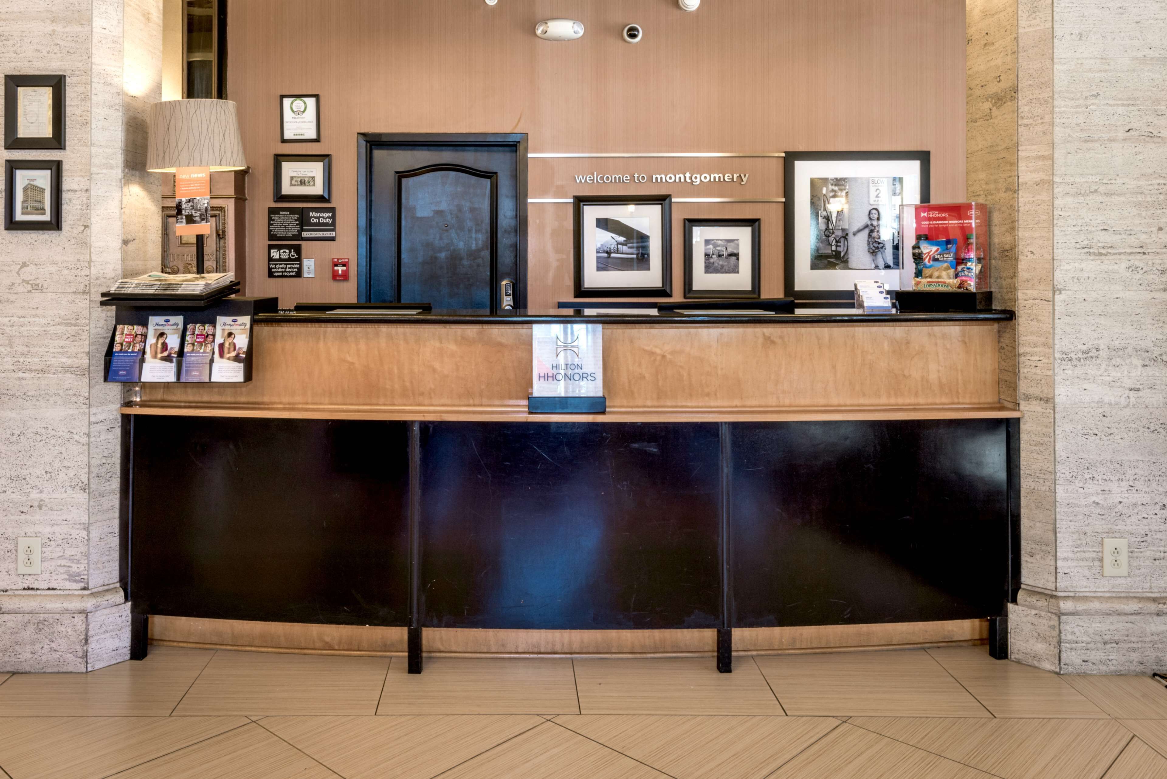 A hotel reception desk with framed pictures, a welcome sign, and a sign for Hilton Honors.