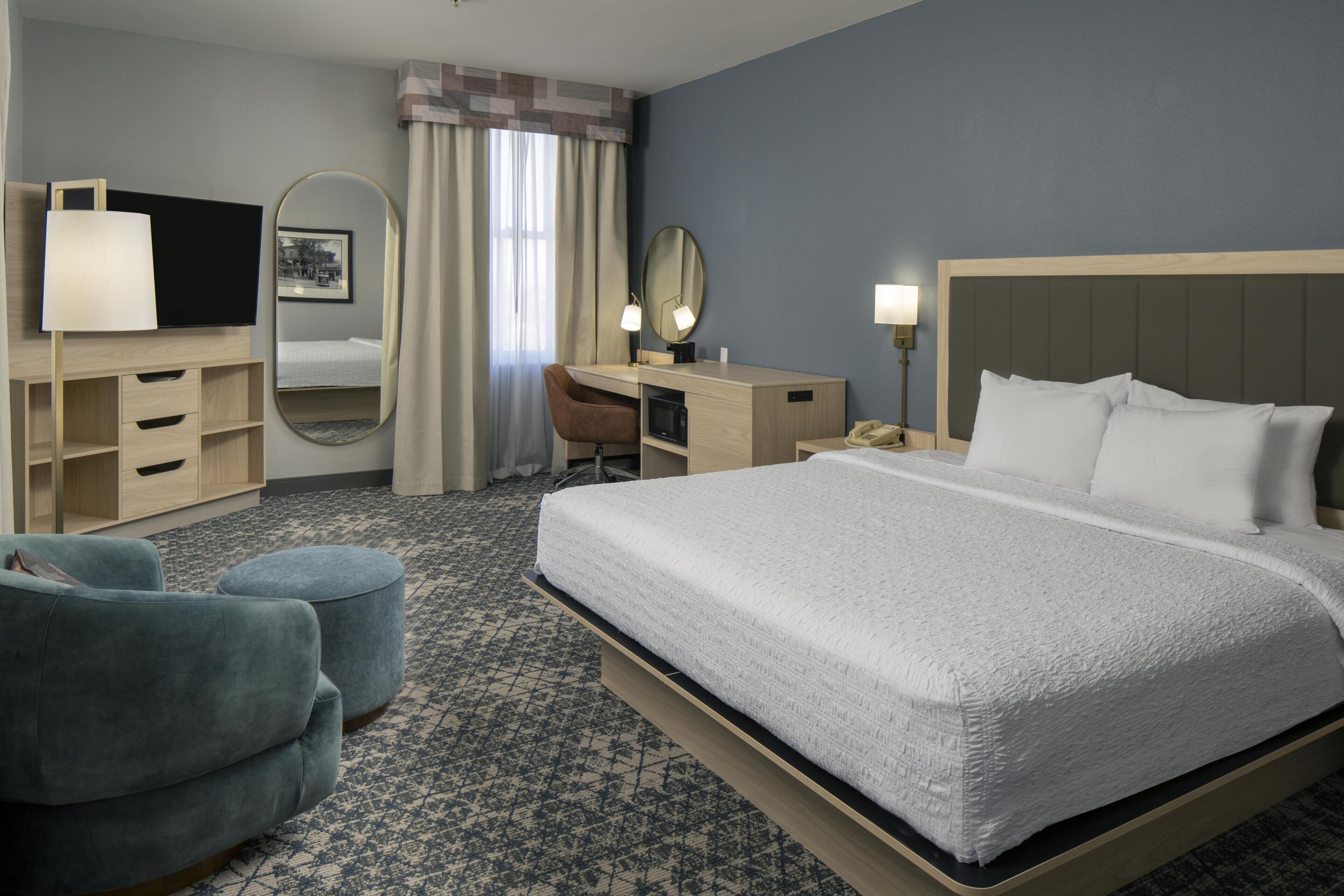 A hotel room with a bed, a desk with a chair, a television, a mirror, and a telephone.