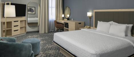 A hotel room with a bed, a desk with a chair, a television, a mirror, and a telephone.