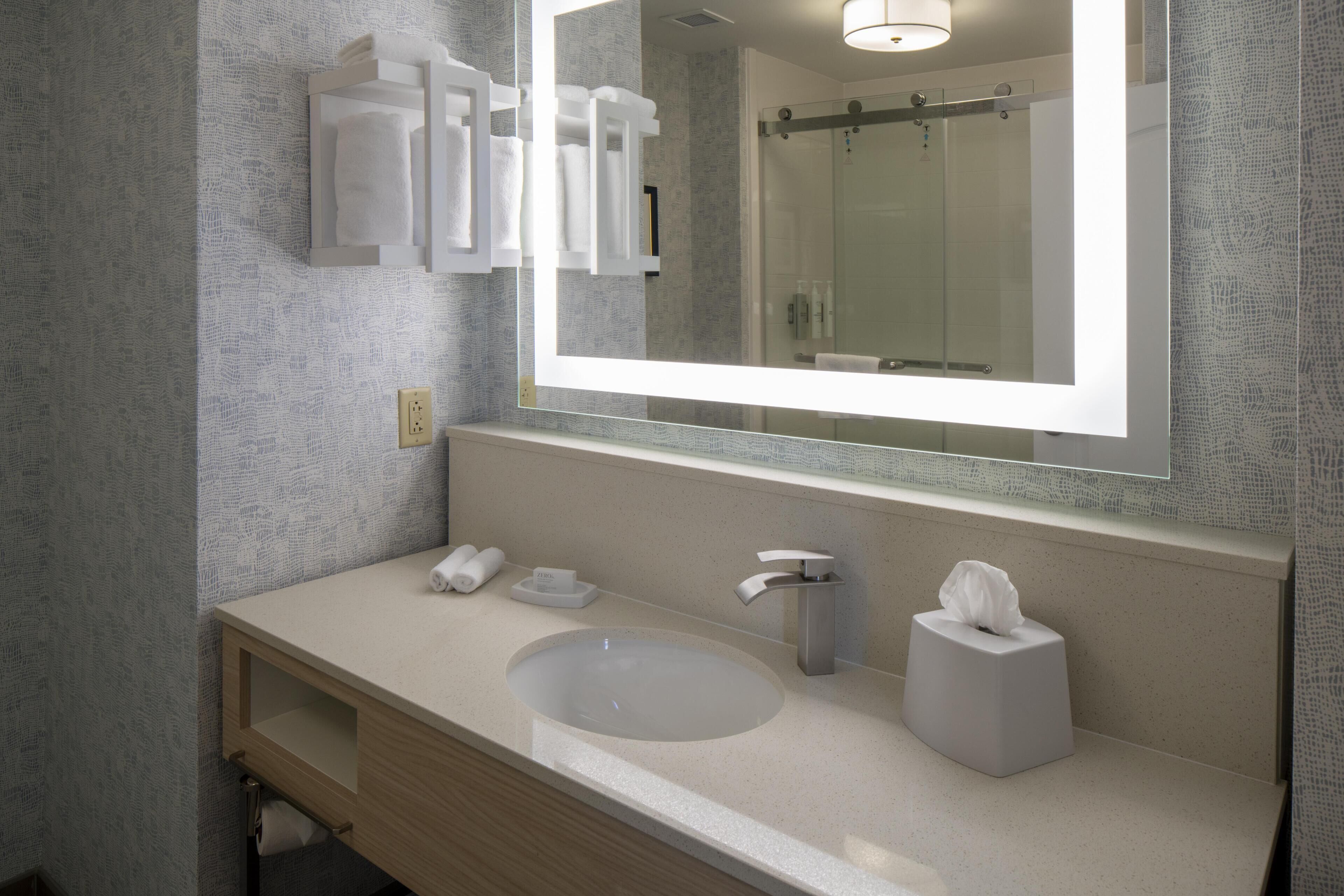Un baño moderno con un espejo grande, un lavabo, un dispensador de toallas y un porta papel higiénico.