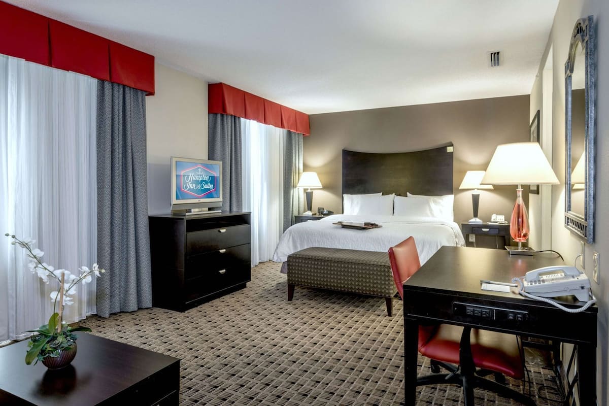 A hotel room with a bed, a desk with a telephone, a television, and a desk lamp.