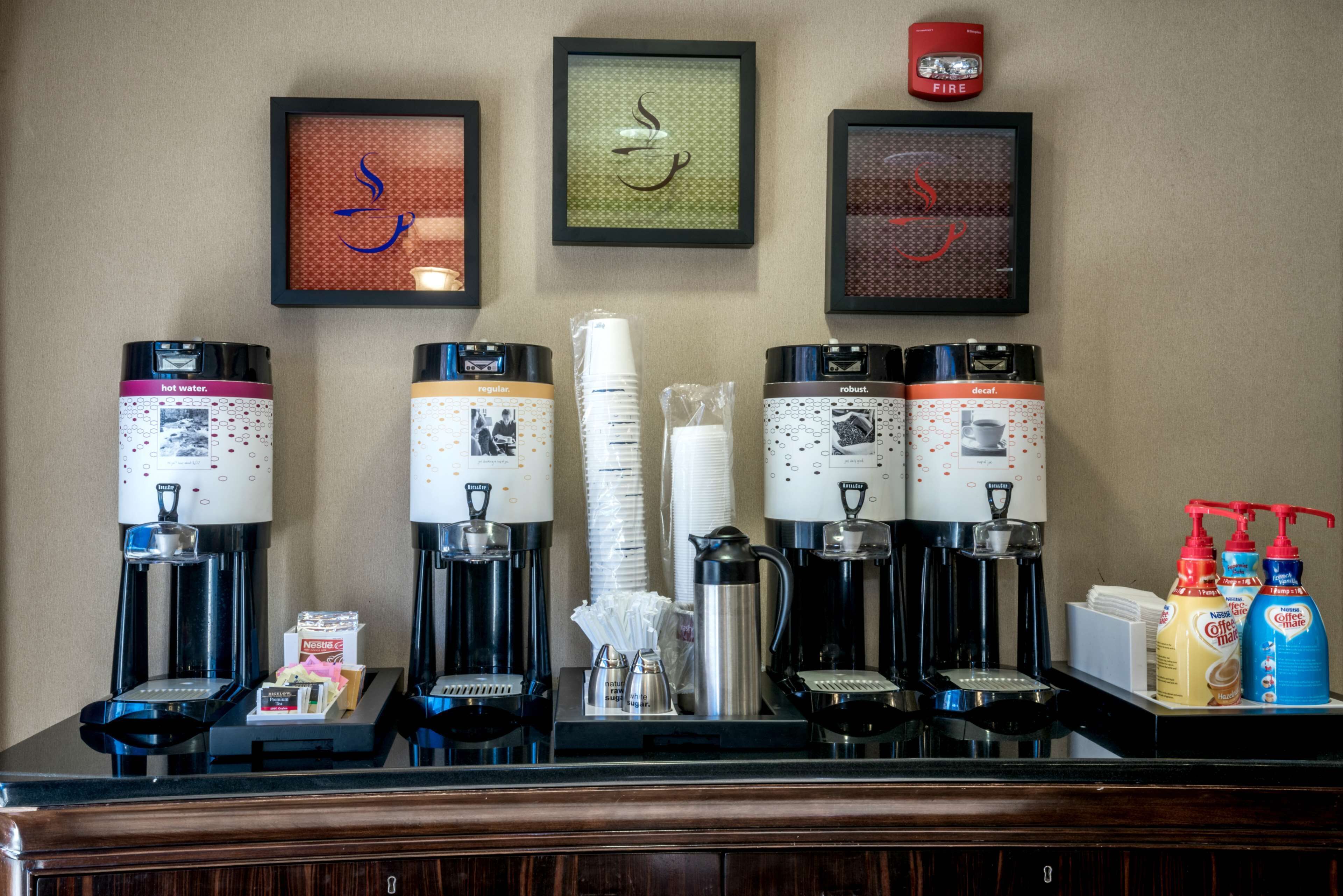 A coffee station with multiple coffee dispensers, disposable cups, and condiments.