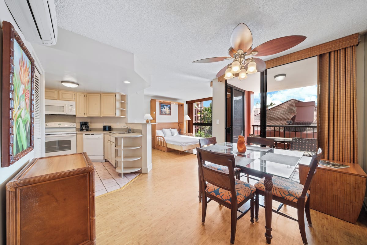 A spacious living area with a dining table, chairs, a ceiling fan, and a view of the outdoors.