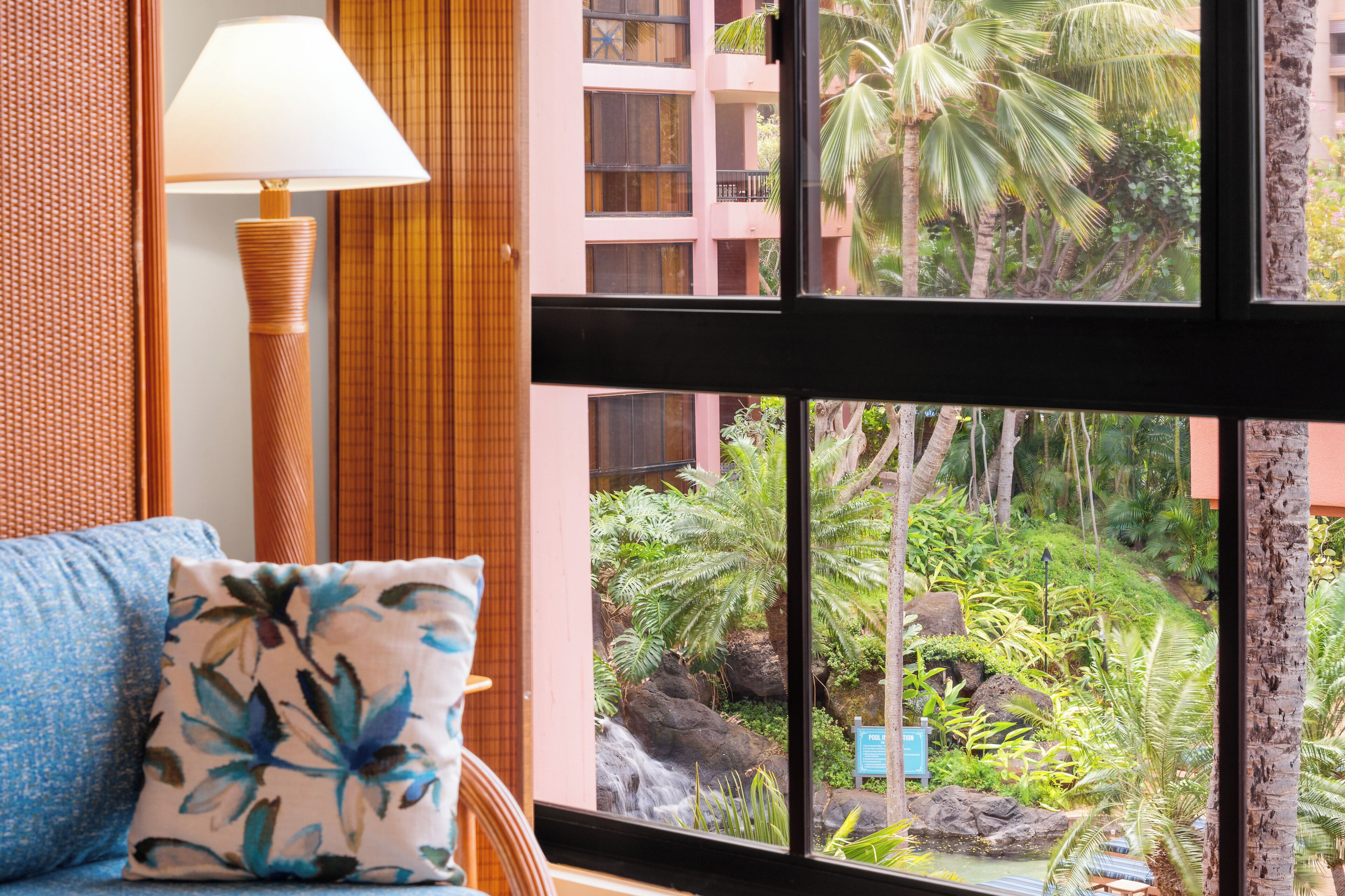 A room with a view of a tropical garden, a blue pillow, and a lamp.