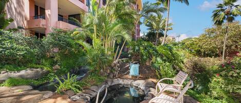 Un área de piscina con jacuzzi, rodeada de abundante vegetación y palmeras, junto a un edificio de varios pisos con balcones.