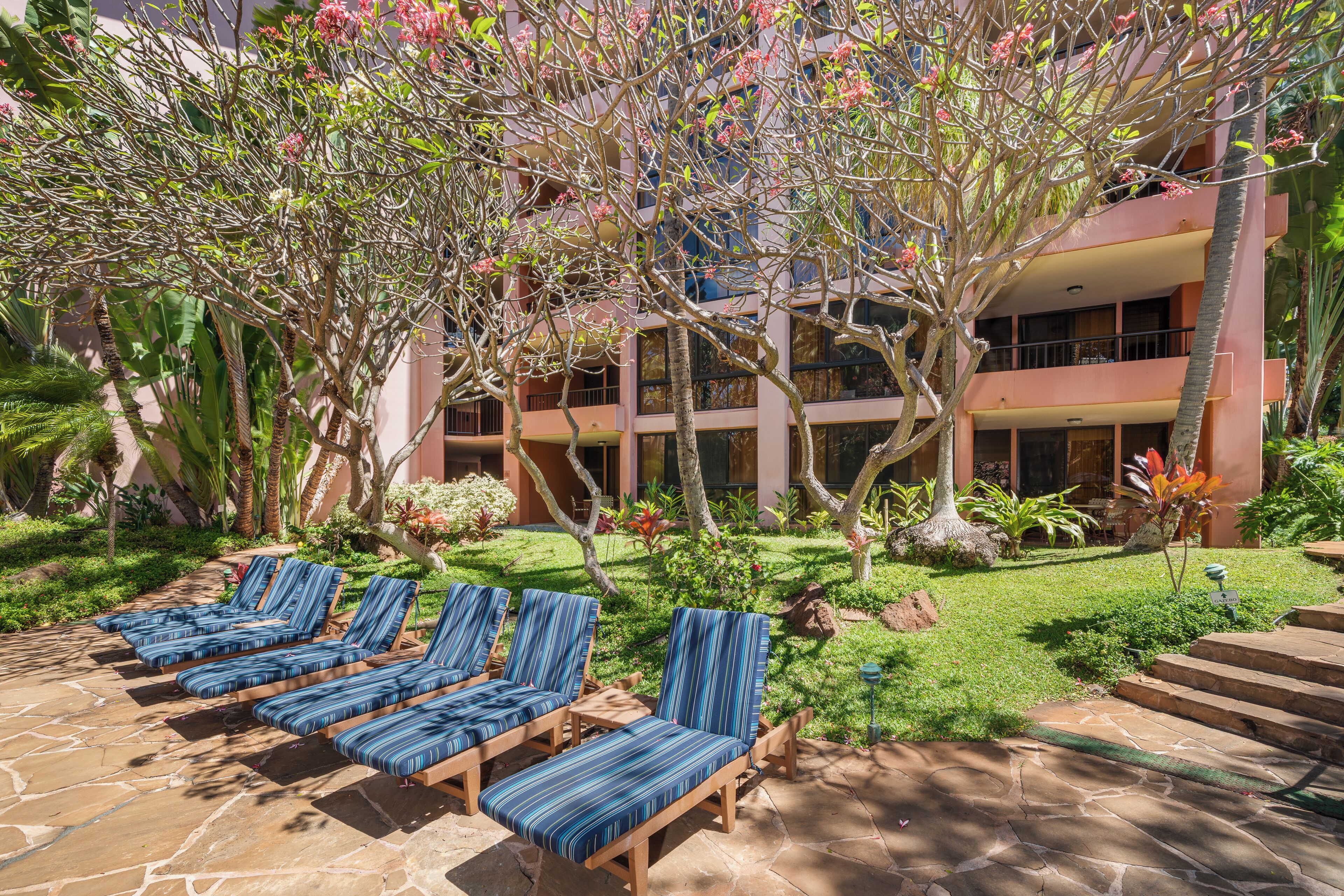 A hotel courtyard with lounge chairs, a stone patio, and a building with balconies.