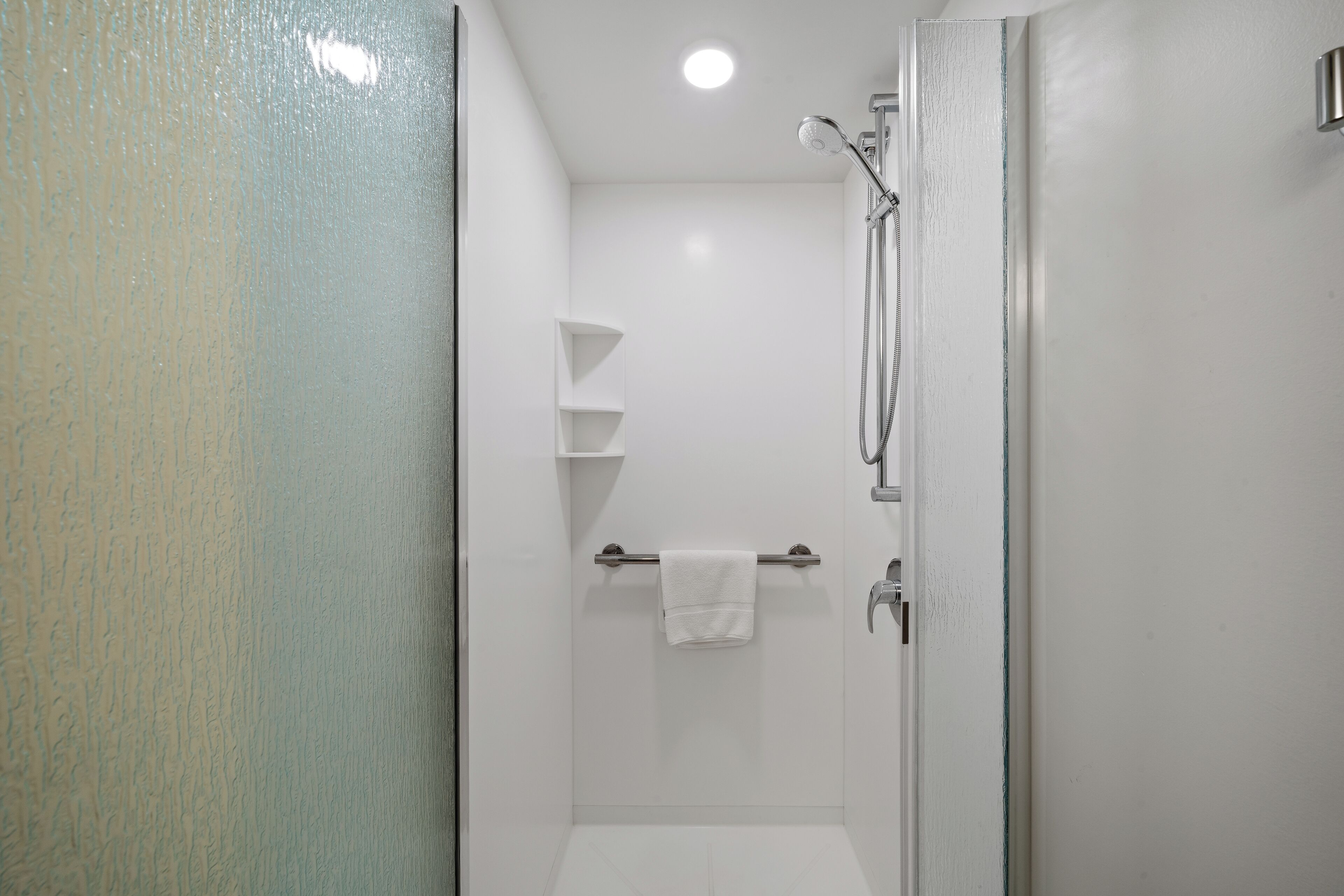 A modern bathroom with a glass shower enclosure, a towel rack, and a shelf.