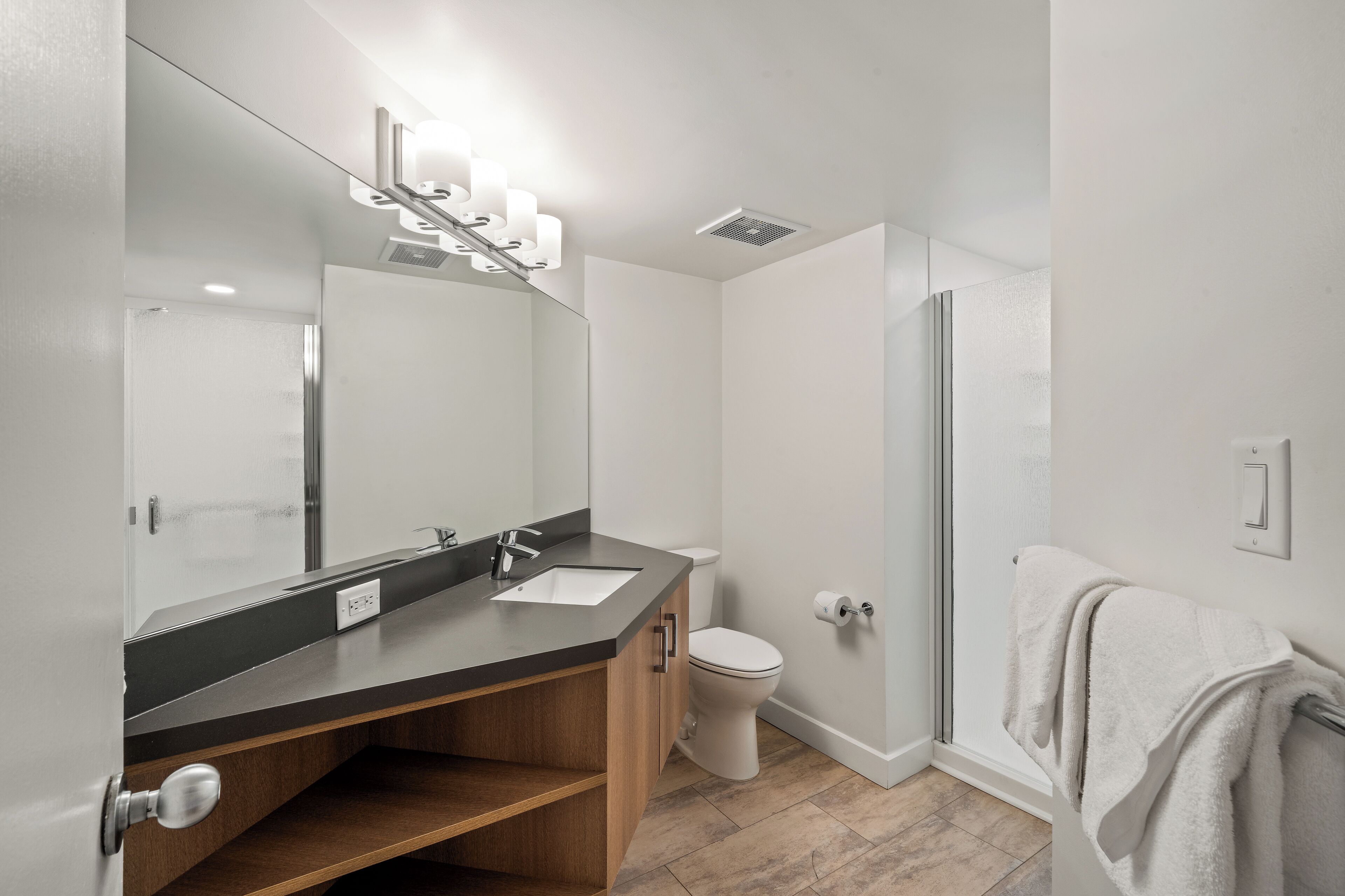 A modern bathroom with a large mirror, a sink, a toilet, and a shower.