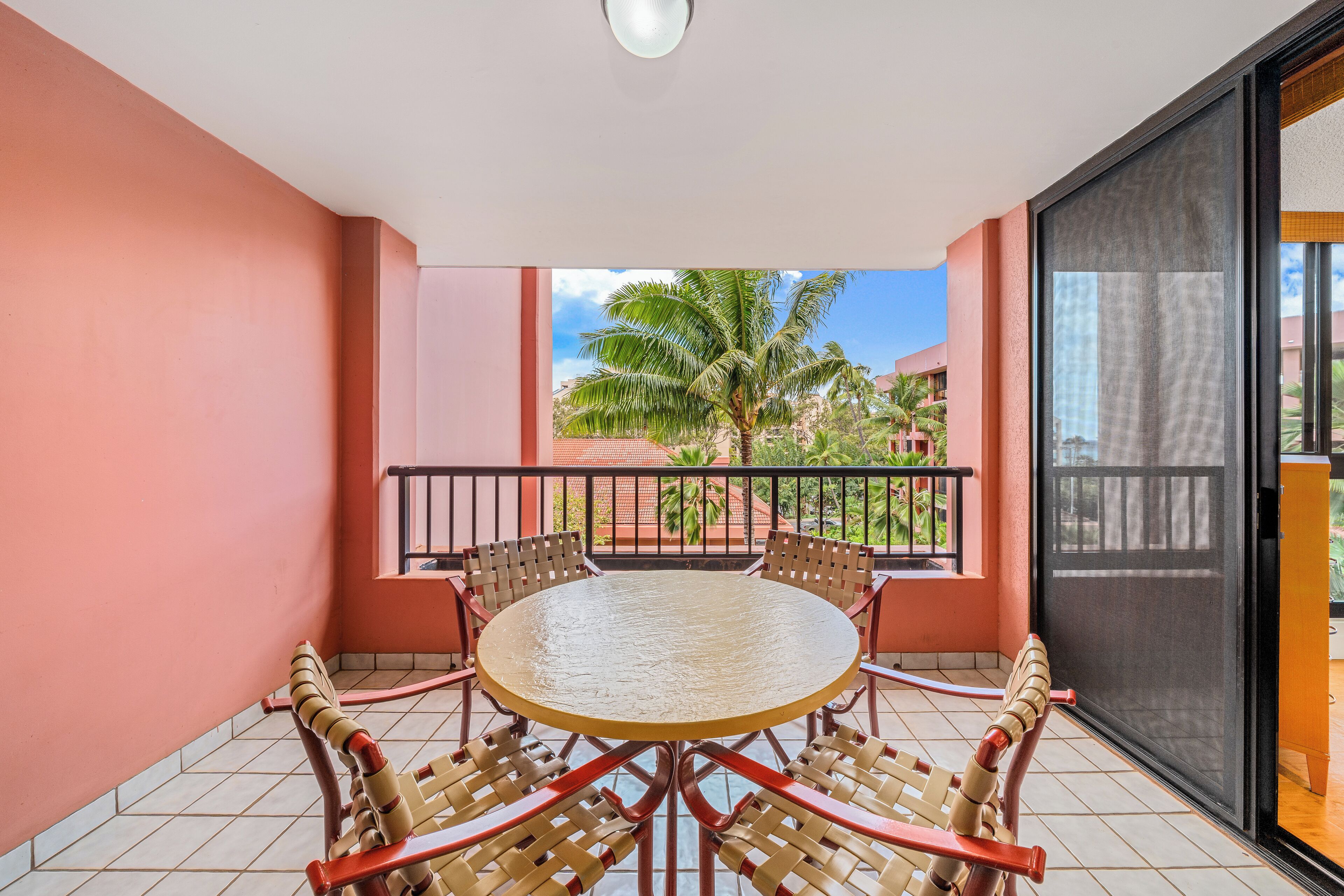 A balcony with a round table and chairs, a view of palm trees, and a building in the background.