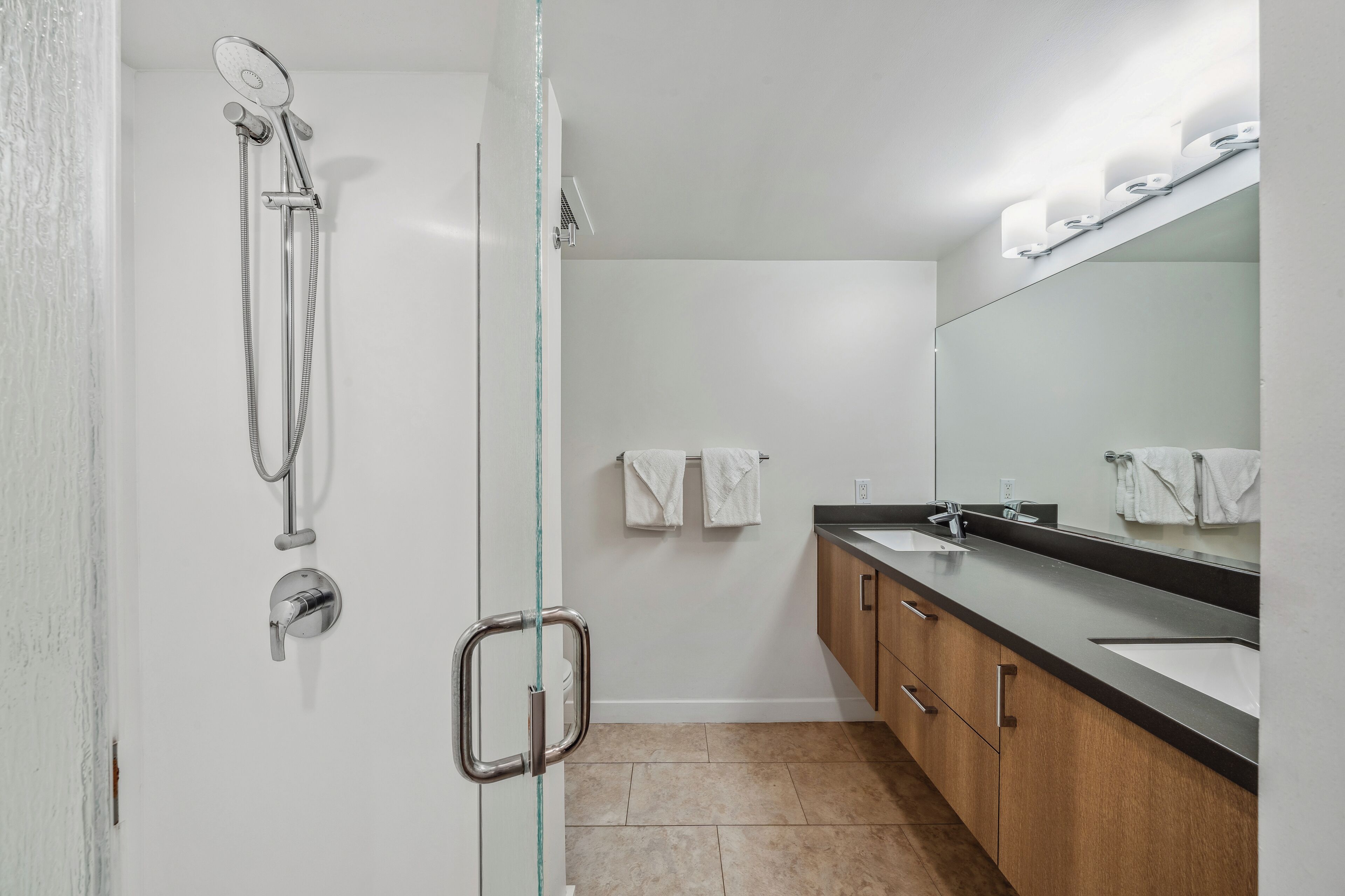 A modern bathroom with a glass shower enclosure, a large mirror, and wooden cabinets.