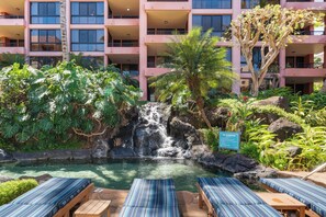 Un hotel con zona de piscina que incluye una cascada, sillas de descanso y abundante vegetación.