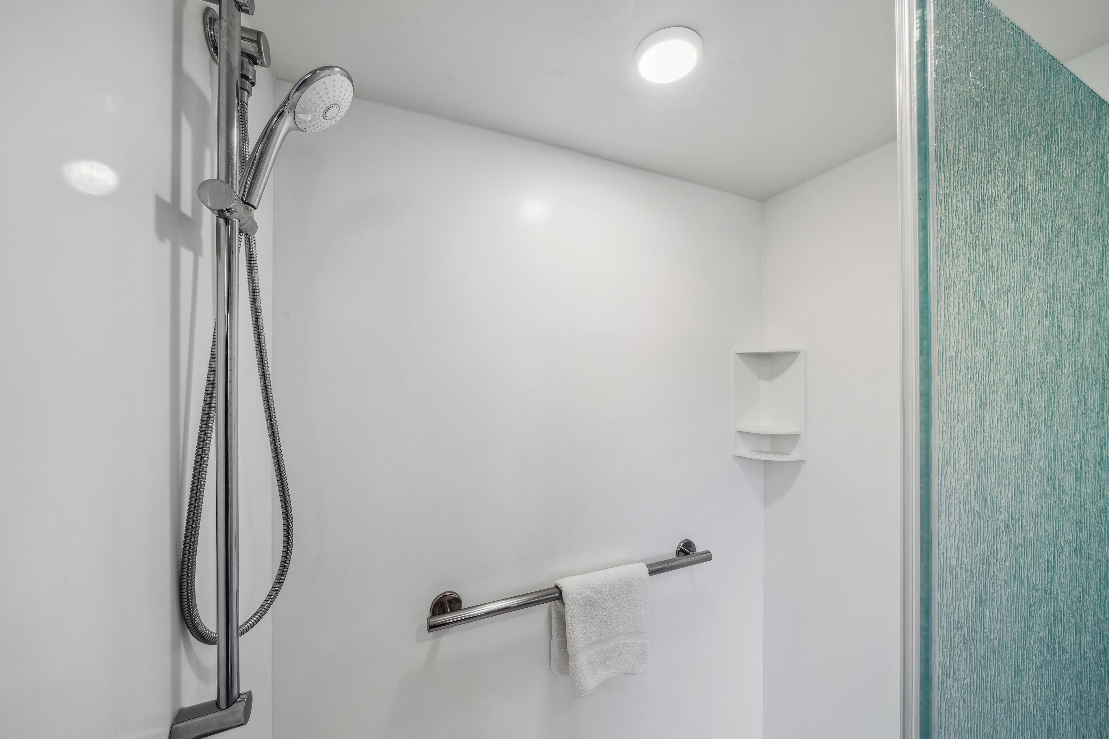 Une salle de bain moderne dotée d’une cabine de douche en verre, d’un porte-serviettes et d’une étagère murale.