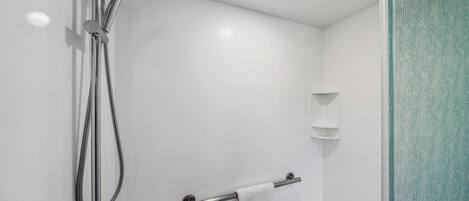 Une salle de bain moderne dotée d’une cabine de douche en verre, d’un porte-serviettes et d’une étagère murale.