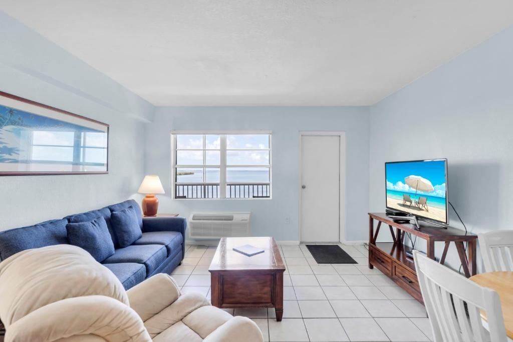 A living room with a sofa, a coffee table, a television on a stand, and a door leading to a balcony.