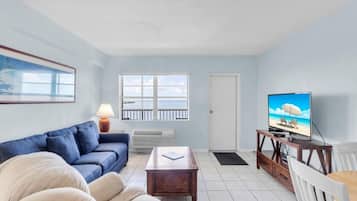 A living room with a sofa, a coffee table, a television on a stand, and a door leading to a balcony.