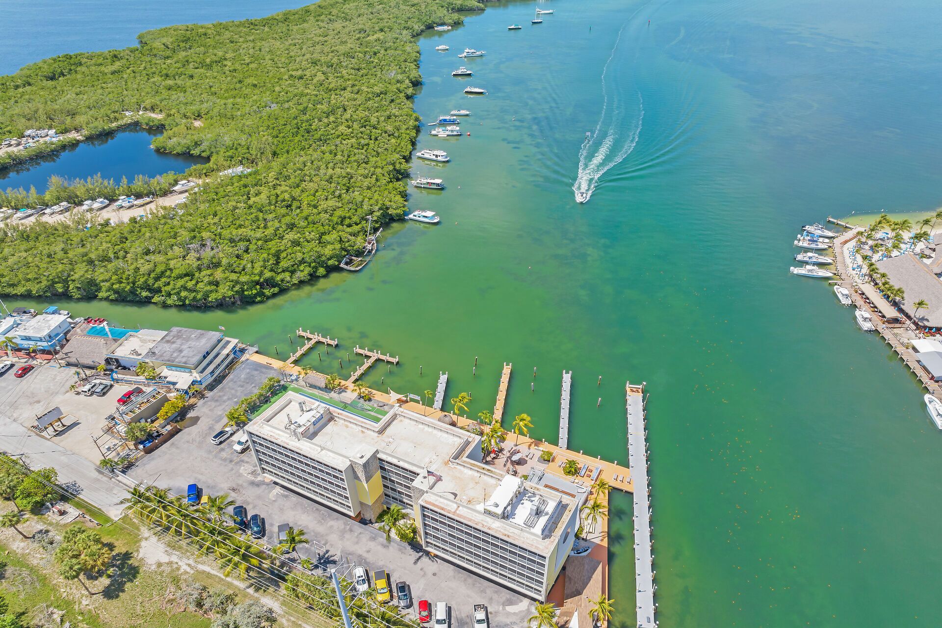 An aerial view of a marina with boats, a dock, and a building with a parking lot.
