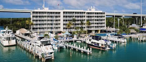 Un port de plaisance avec des bateaux amarrés, un immeuble à plusieurs étages doté de balcons et un pont en arrière-plan.