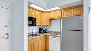 Una cocina compacta con armarios de madera, un microondas negro, un refrigerador blanco y una cafetera.