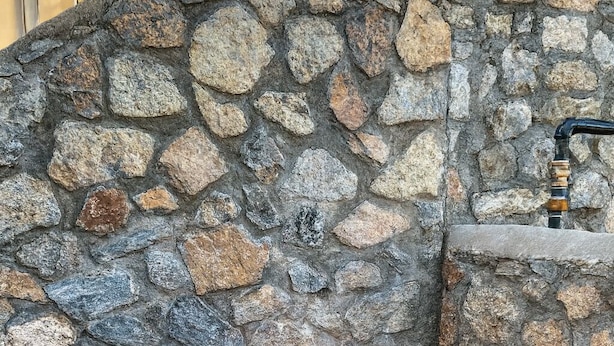 A stone fire pit with a circular stone surround and a flat stone top, set against a stone wall. - Crown Point Resort (Ruidoso)