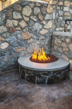 A stone fire pit with a circular stone surround and a flat stone top, set against a stone wall. - Crown Point Resort (Ruidoso)