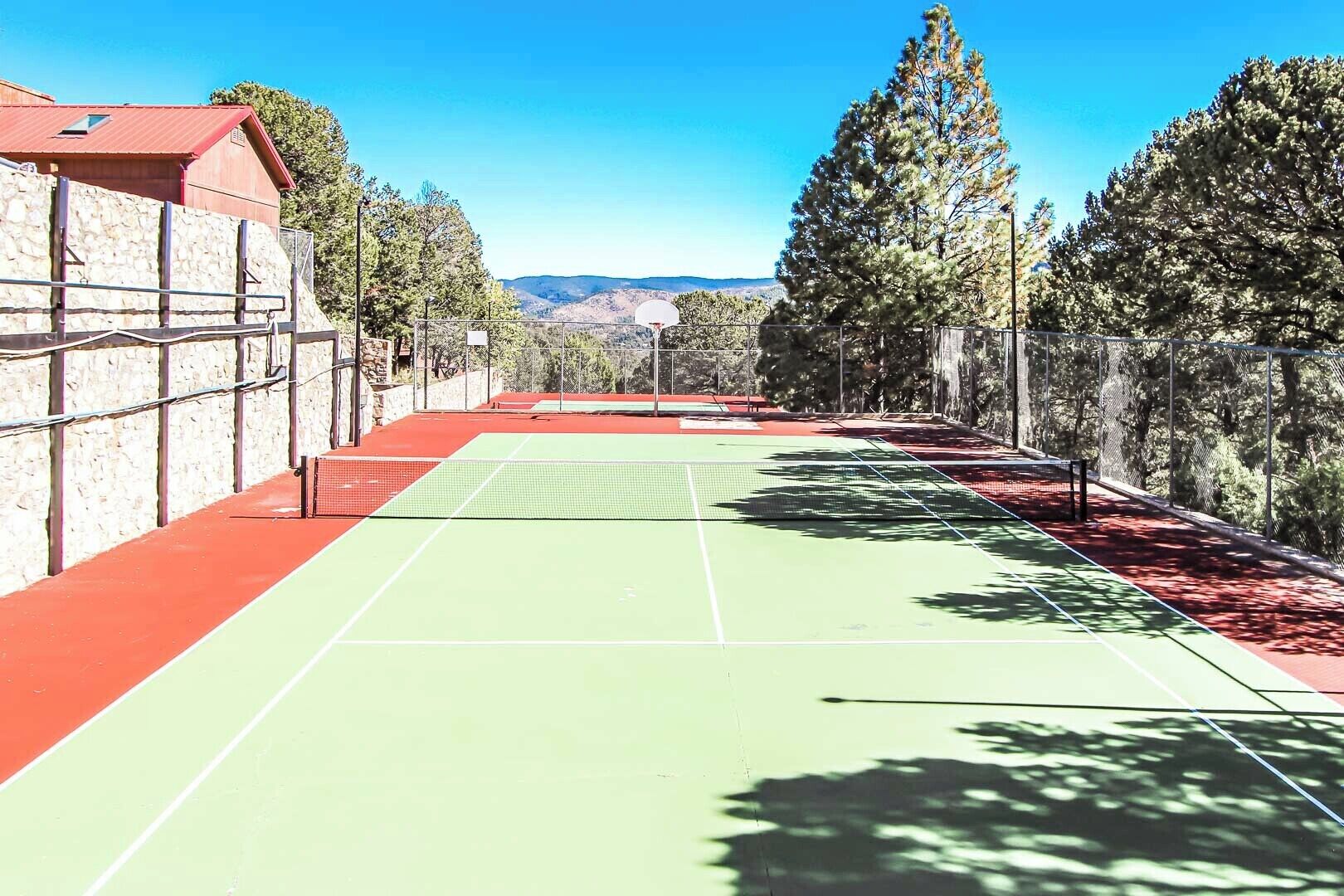 Een tennisbaan buiten met een stenen muur aan de ene kant en bomen aan de andere kant.