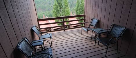 A wooden deck with metal chairs and tables, overlooking a forested area.