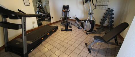 A gym with a treadmill, elliptical, stationary bike, and weight bench.