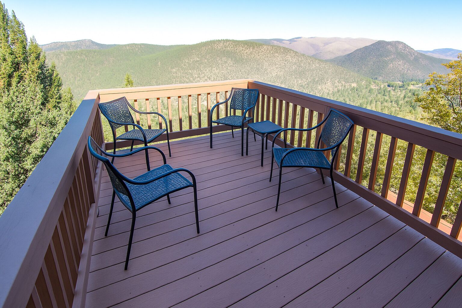 Eine Holzterrasse mit Metallstühlen und -tischen, mit Blick auf eine gebirgige Landschaft.