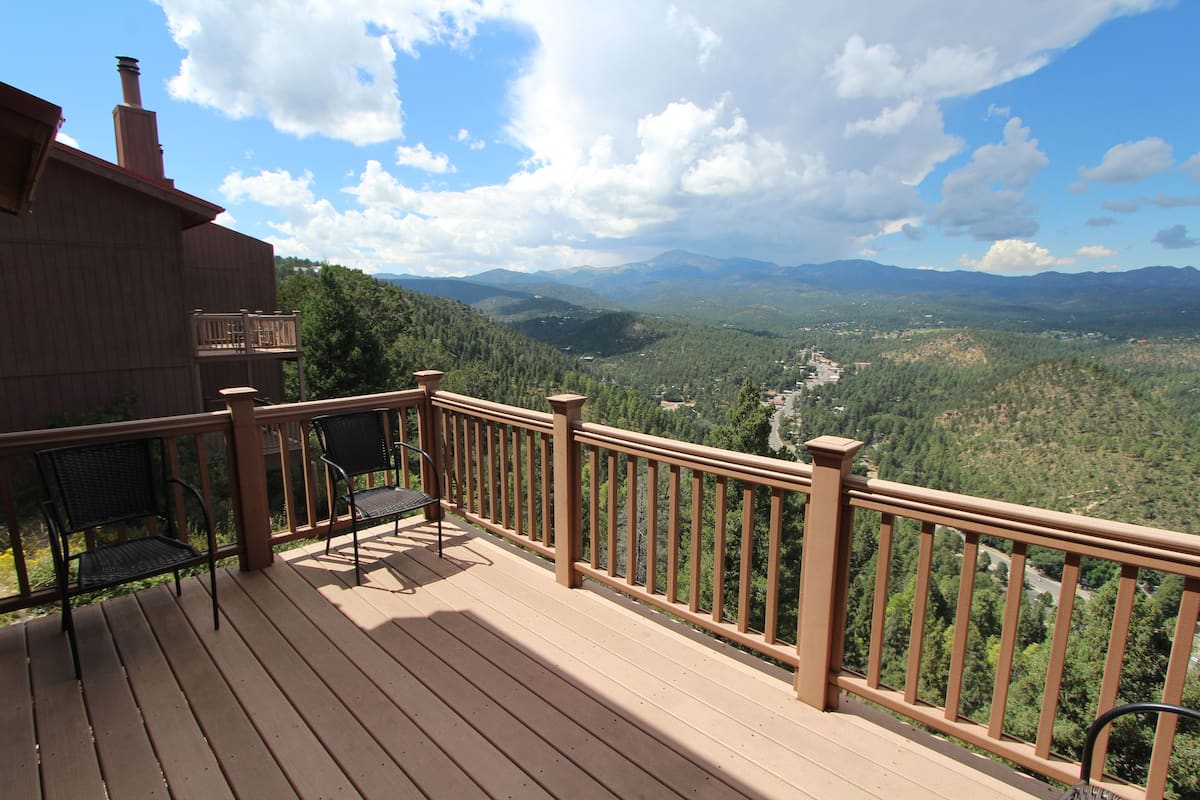 A wooden deck with a railing, two chairs, and a table.