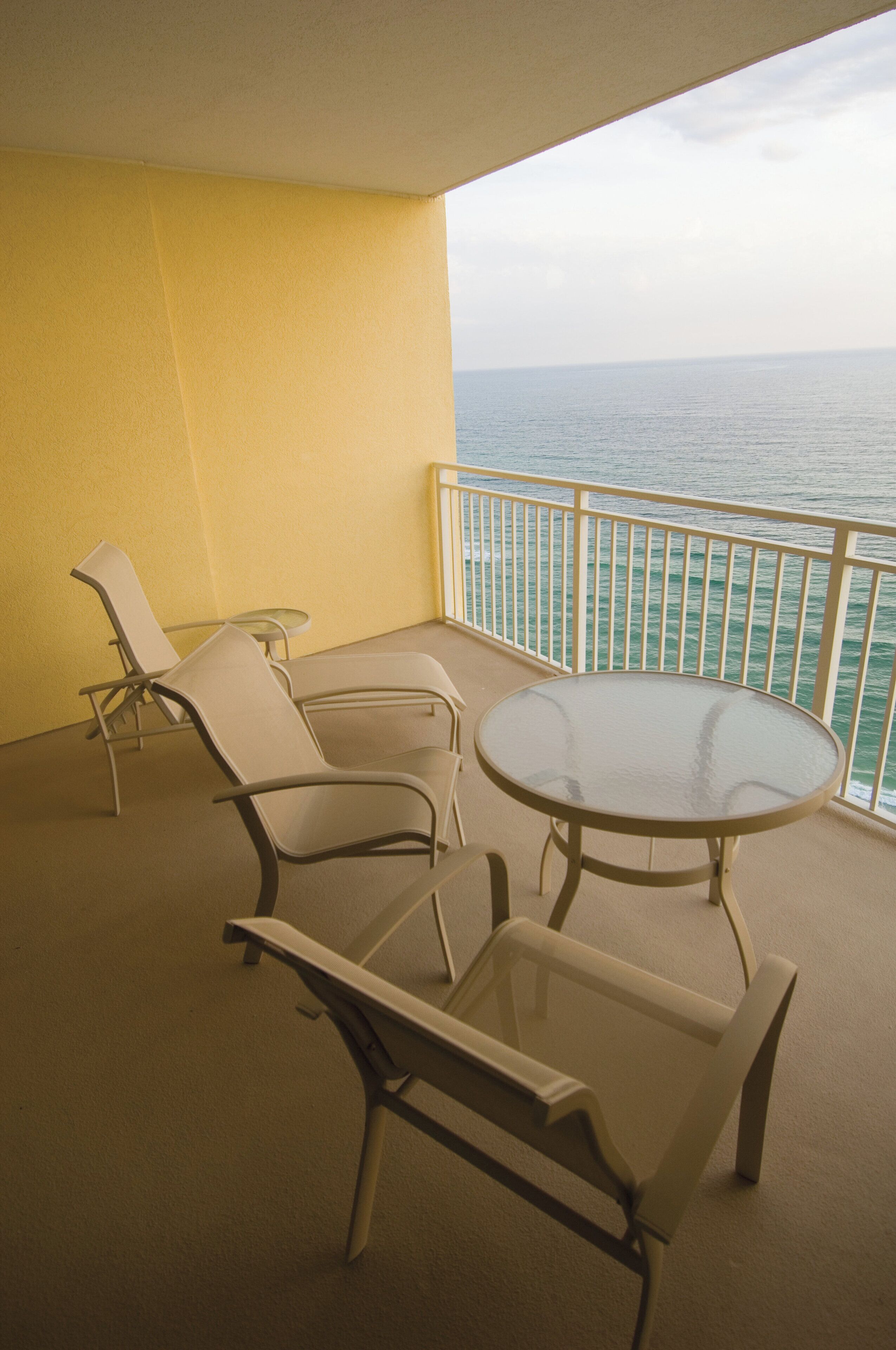 A balcony with a round glass table and two chairs, overlooking the sea.