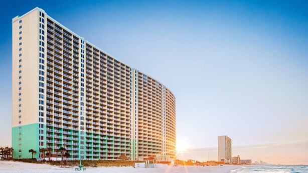 A beachfront hotel with multiple floors, a sandy beach, and the ocean.