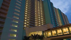 A high-rise hotel with multiple floors, a glass entrance, and a palm tree-lined driveway.