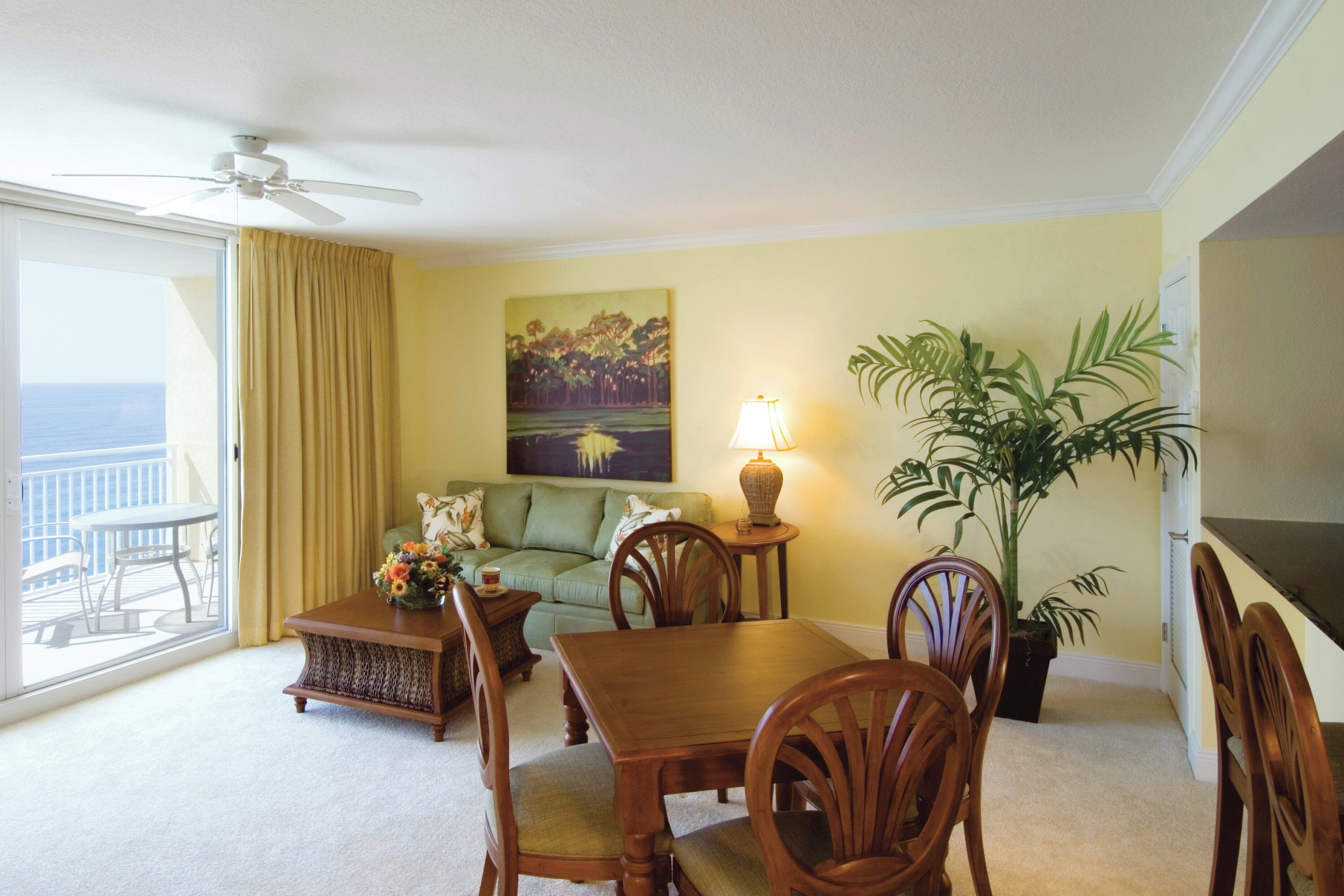 A room with a dining table, chairs, a sofa, a lamp, a plant, and a painting on the wall.