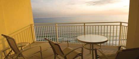 A balcony with a view of the ocean at sunset, featuring a round table and four chairs.