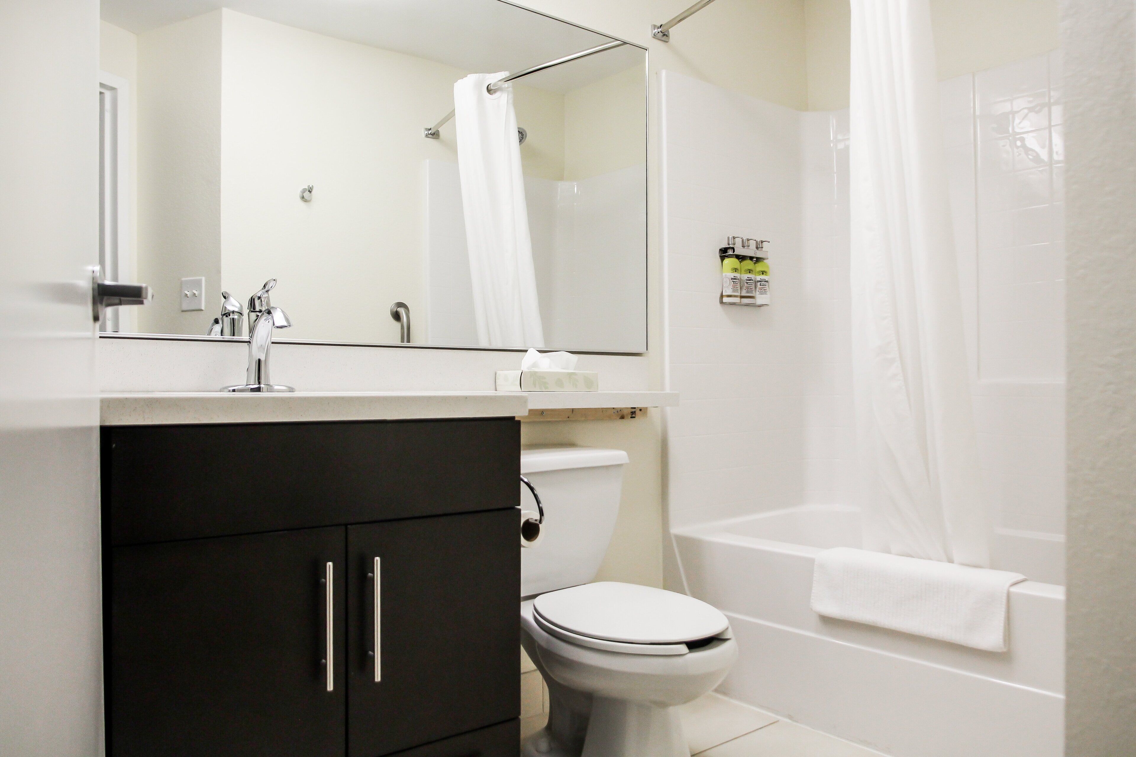 A bathroom with a toilet, sink, mirror, and shower area.