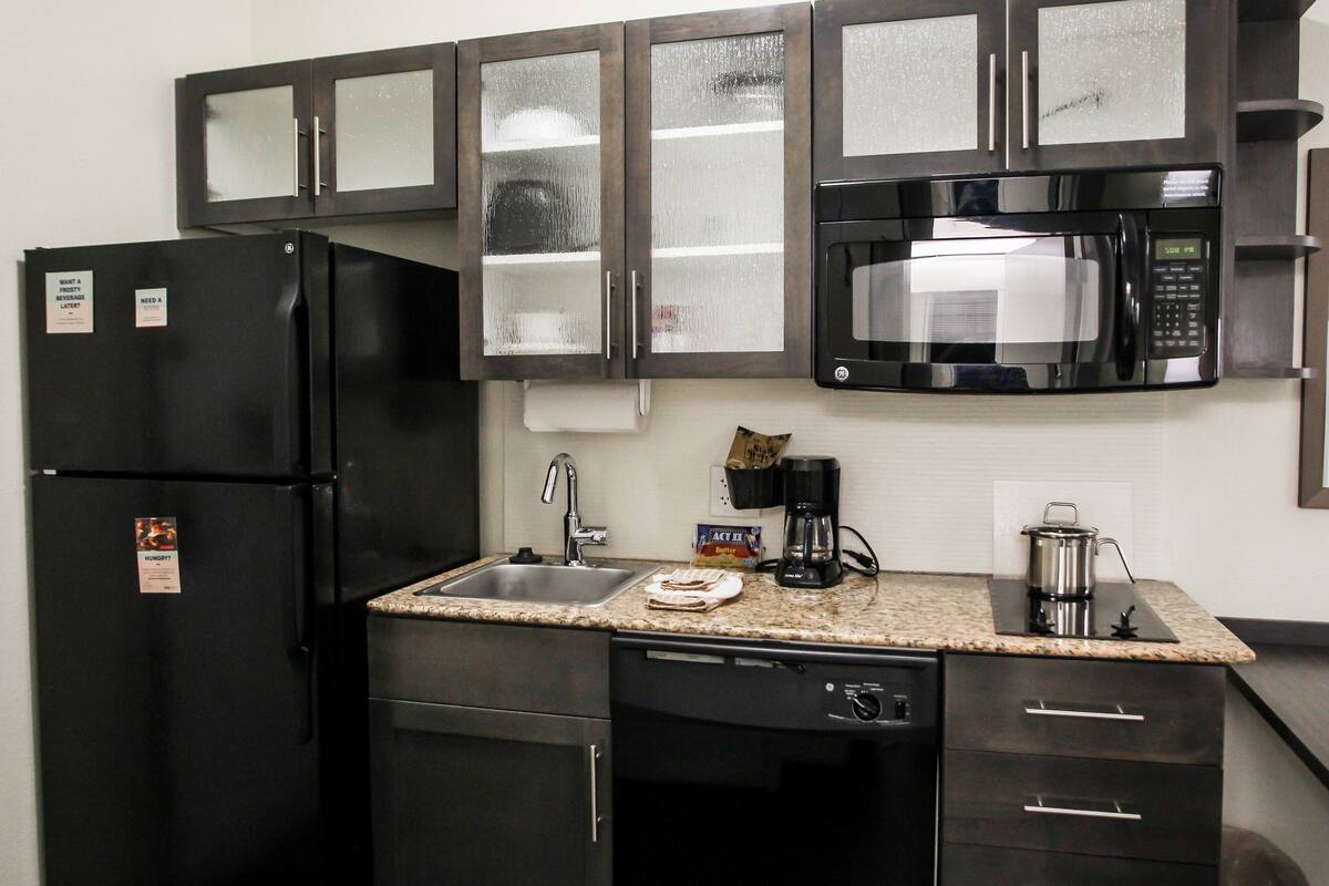 A compact kitchen with a black refrigerator, stainless steel microwave, and granite countertop.