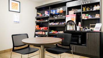 A coffee shop with a round table and two chairs, shelves stocked with snacks and a coffee machine.