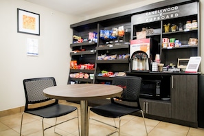 Un café avec une table ronde et deux chaises, des étagères remplies d’en-cas et une machine à café.