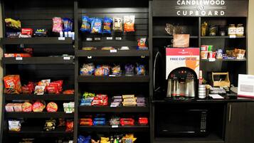 A snack and coffee station with various packaged snacks, a coffee machine, and a sign offering a free cup of joe.