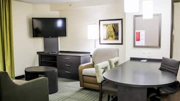 A hotel room with a flat-screen TV, a desk, a conference table, and a chair.