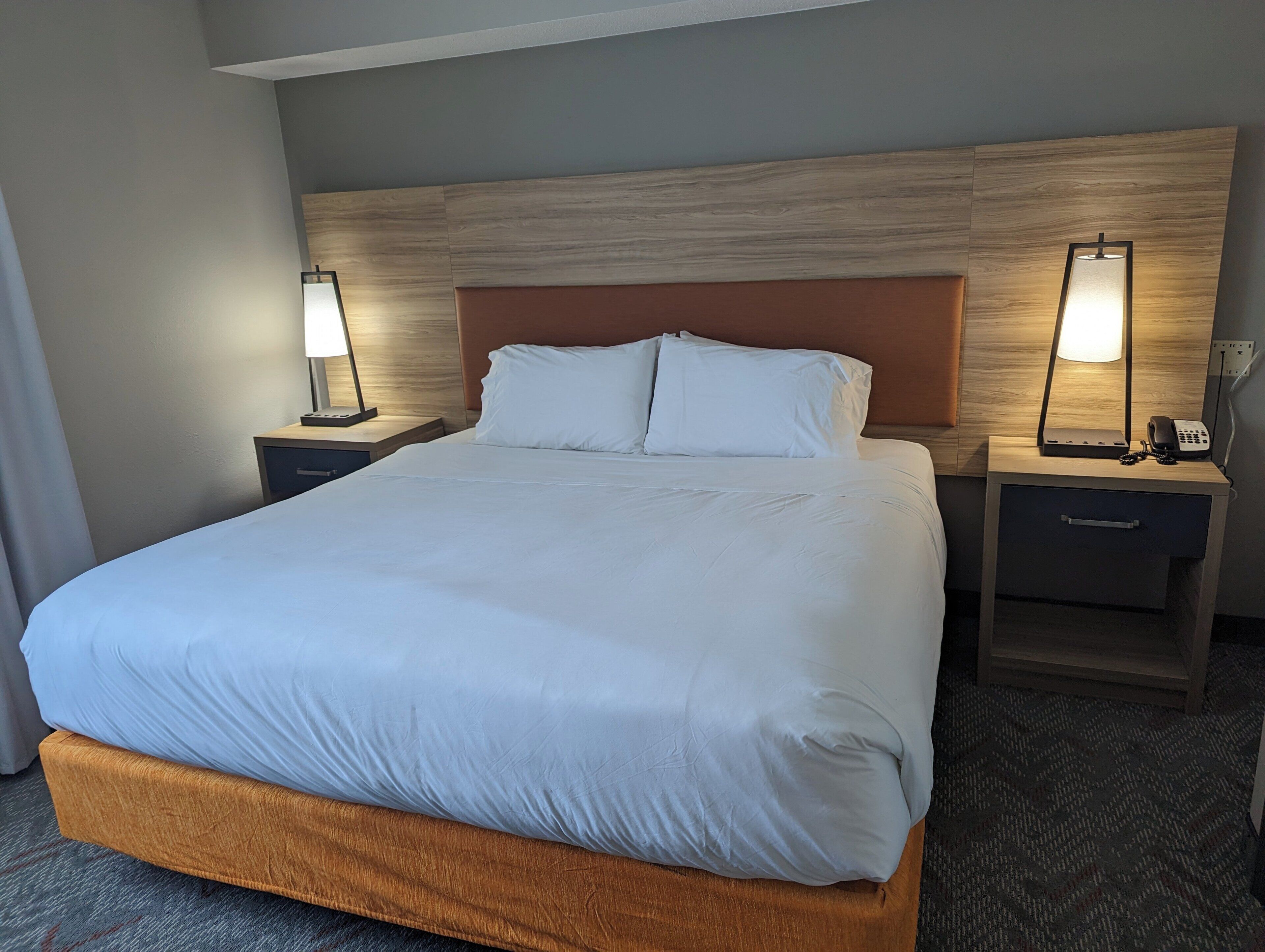 Ein Hotelzimmer mit einem großen Bett, zwei Nachttischen, einem Holzkopfstück und zwei Wandlampen.