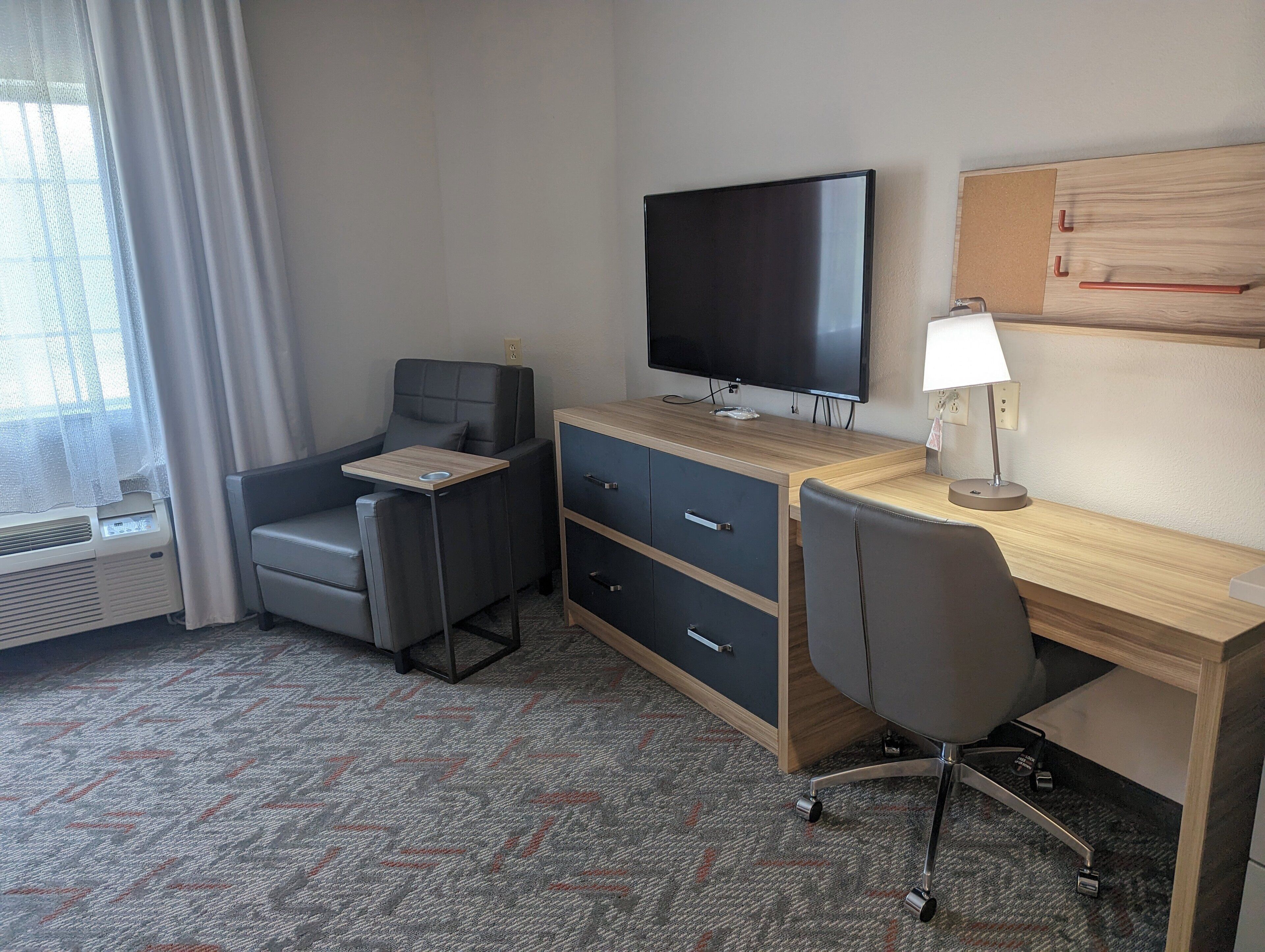 A hotel room with a desk, chair, television, and a lamp.
