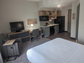 A hotel room with a bed, a desk, a TV, a chair, a small kitchenette, and a door. - Candlewood Suites Wilson by IHG (Wilson)