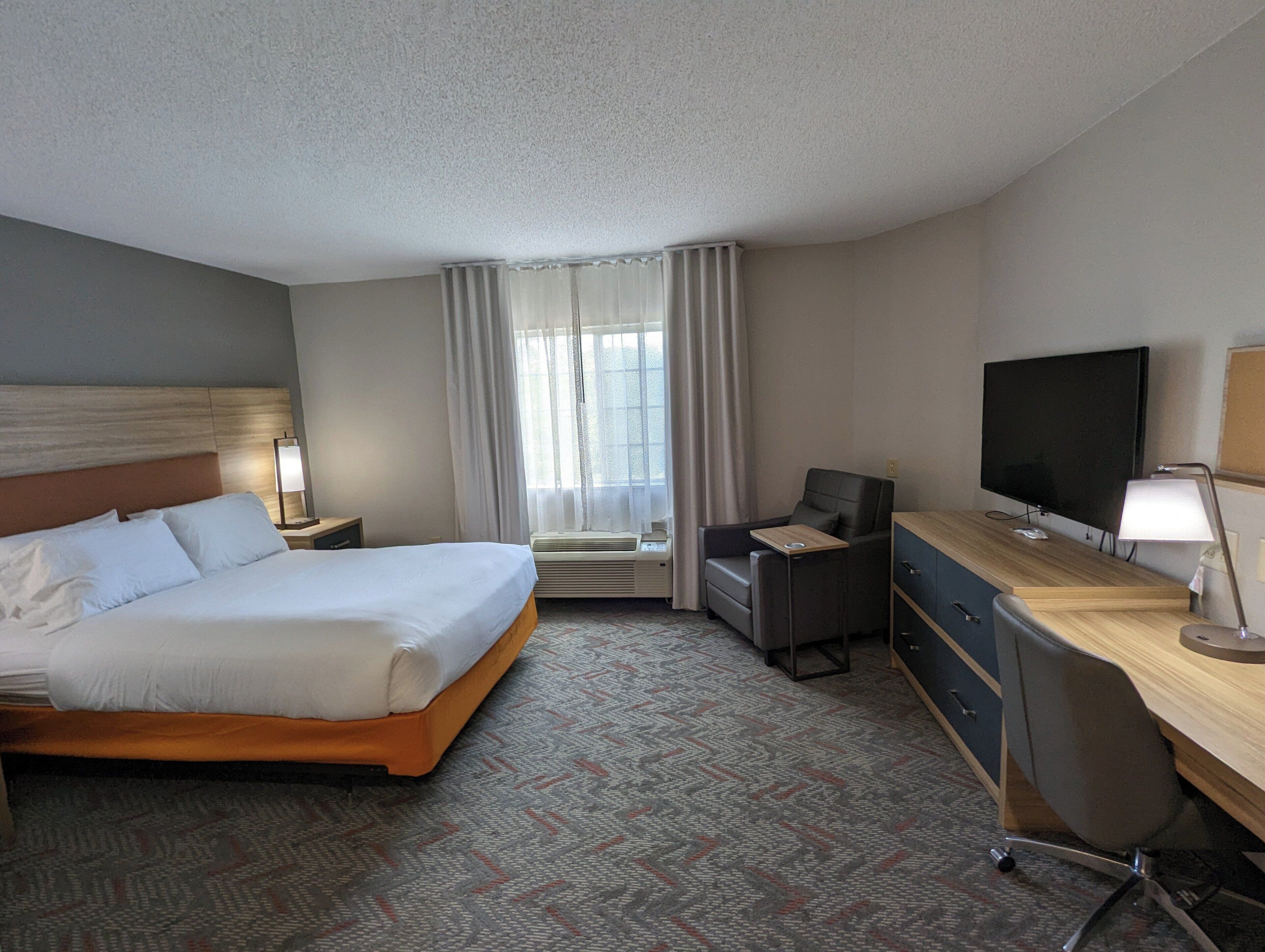 A hotel room with a bed, desk, chair, television, and a window with curtains.