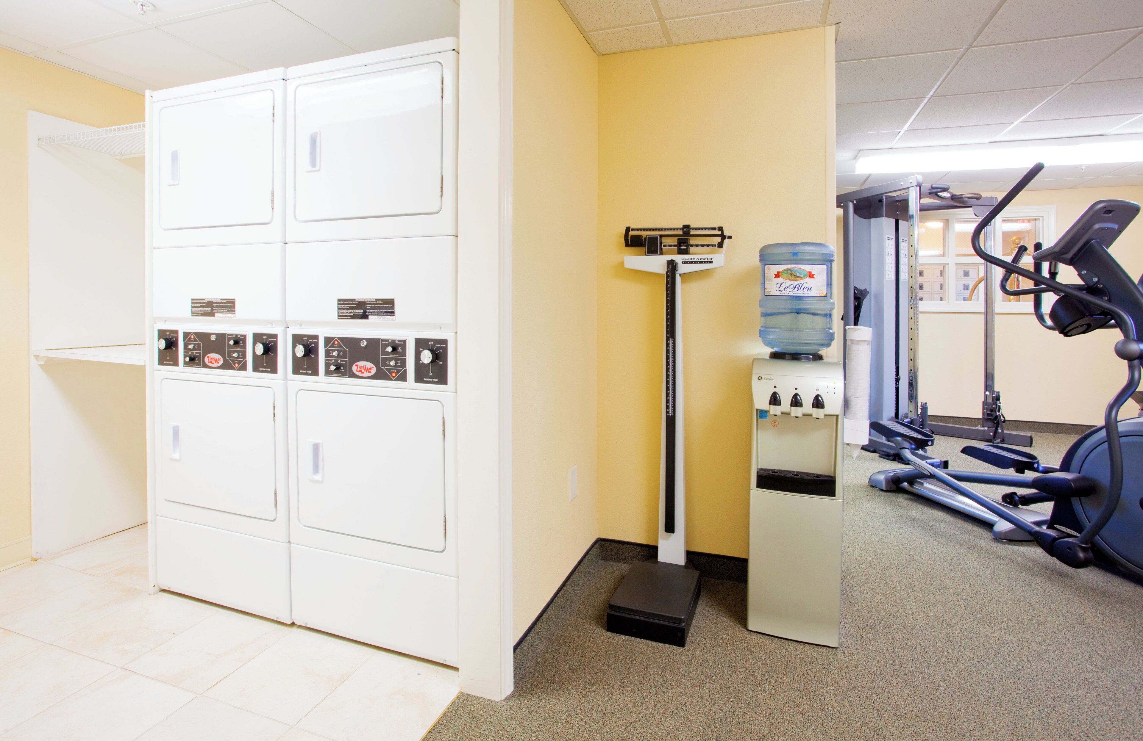 A laundry room with stacked washers and dryers, a scale, and a water dispenser.
