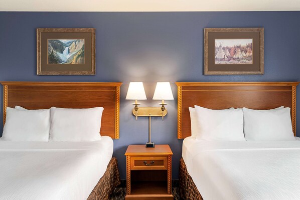 Una habitación de hotel con dos camas, una mesita de noche con dos lámparas y dos cuadros en la pared.