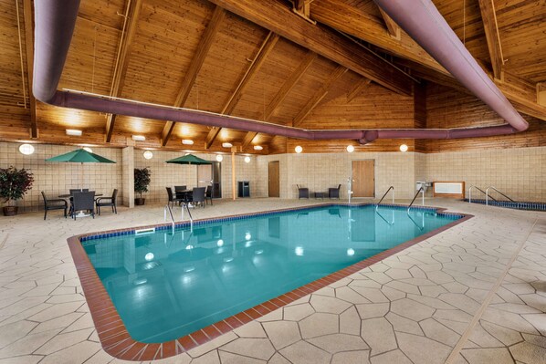 An indoor swimming pool with a wooden ceiling, tiled walls, and a hexagonal floor pattern.