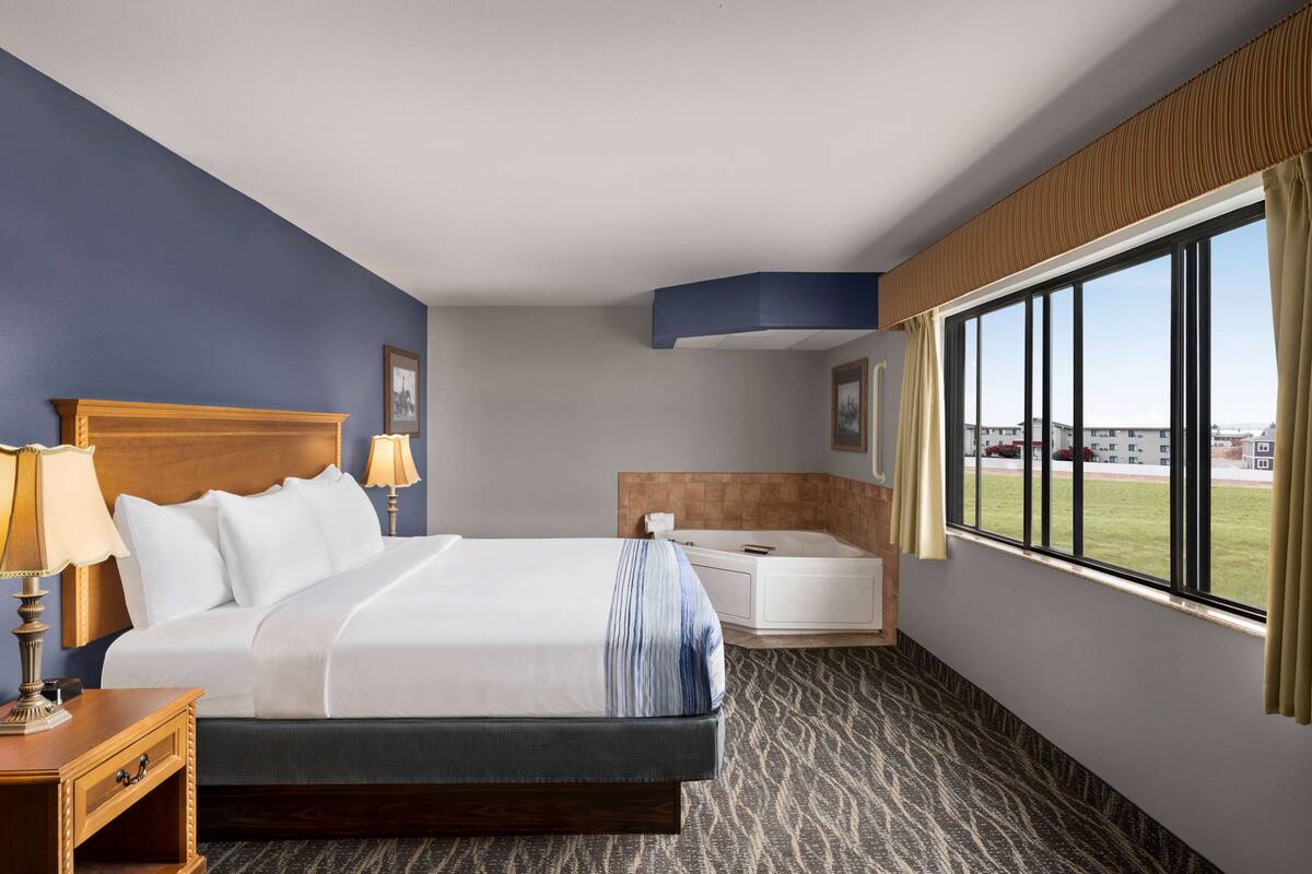 Ein Hotelzimmer mit einem großen Bett, einer Sitzecke inklusive Sessel und Tisch, einer Badewanne und einem großen Fenster mit Aussicht.