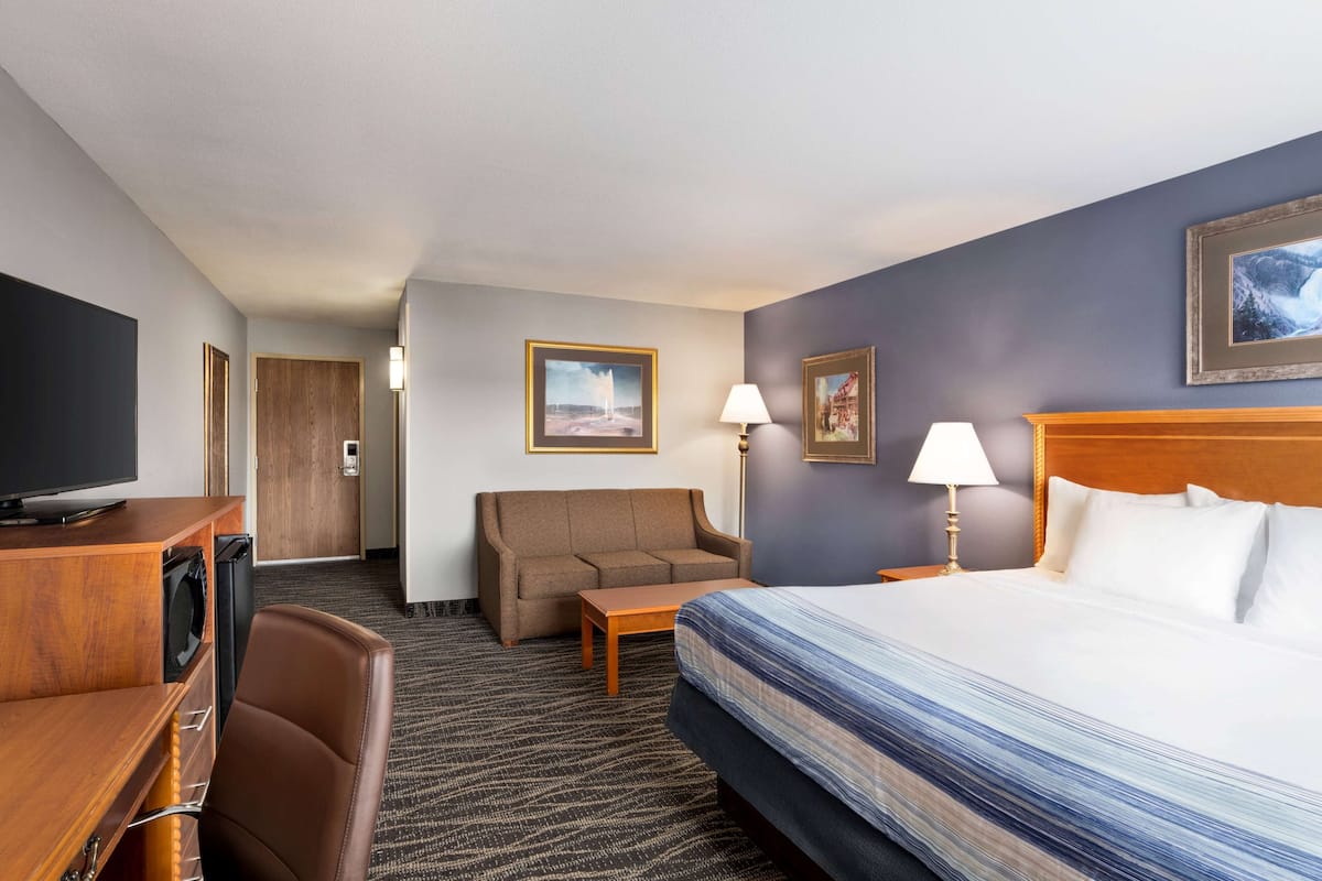 Ein Hotelzimmer mit Bett, Fernseher, Sofa, Schreibtisch und Lampe.